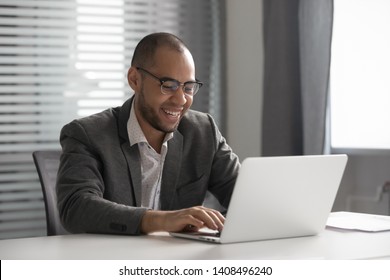 Smiling african american businessman in suit working on computer sit at office desk, happy mixed race worker entrepreneur typing email on laptop communicating online using software for business - Shutterstock ID 1408496240