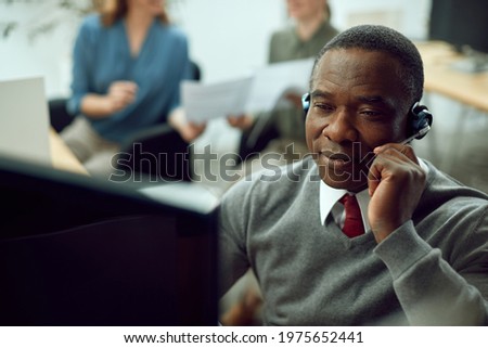 Smiling African American businessman talking over headset while having video call over desktop PC in the office.