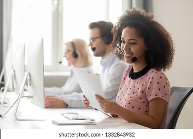 Smiling african american businesswoman call center operator agent wearing headset holding papers reading clients contacts working in customer service support helpdesk business office with colleagues