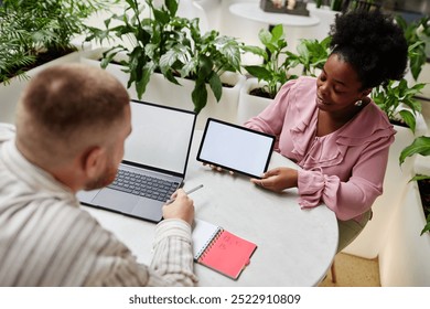 Smiling African American businesswoman holding digital tablet with white mockup screen presenting male colleague work project at business meeting in cafe at modern office center - Powered by Shutterstock