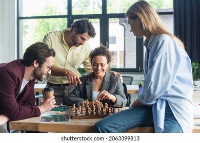 Smiling african american businesswoman playing chess near colleague pointing with finger and business people in office - Powered by Shutterstock