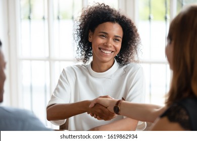 Smiling African American Businesswoman Shaking Hand Of Client At Meeting, Friendly Realtor Broker Manager Making Deal With Family, Customers Purchasing New House, Taking Loan Or Mortgage In Bank