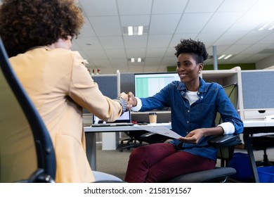 Smiling african american businesswoman shaking hands with hispanic female colleague in cubicle. unaltered, business, agreement, teamwork and modern office concept.