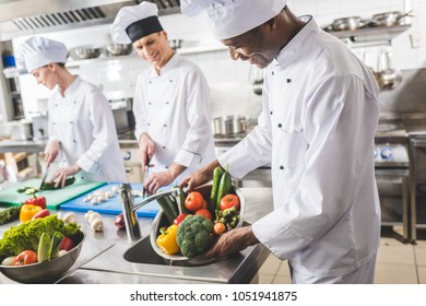 Smiling African American Chef Washing Vegetables At Restaurant Kitchen