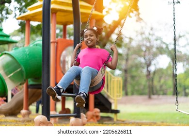 Smiling African American Child Girl Playing On Swing At The Playground. Happy Girl Having Fun On Swing Outdoor