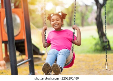 Smiling African American child girl playing on swing at the playground. Happy girl having fun on swing outdoor - Powered by Shutterstock