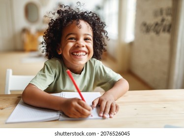 Smiling African American Child School Boy Doing Homework While Sitting At Desk At Home, Happy Mixed Race Kid Practicing Handwriting In Notebook, Learning To Write In Exercise Book