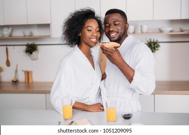 Smiling African American Couple Eating Toast With Jam In Kitchen