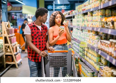 Smiling African American Couple With Shopping Trolley Choosing Food In Supermarket