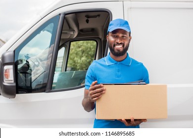 smiling african american delivery man holding cardboard box and looking at camera