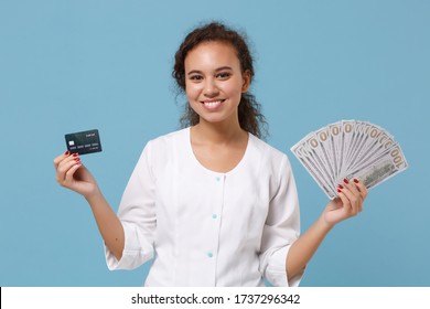 Smiling African American Doctor Woman Isolated On Blue Background. Female Doctor In Medical Gown Hold Fan Of Cash Dollar Money, Credit Card. Healthcare Personnel Medicine Concept. Mock Up Copy Space