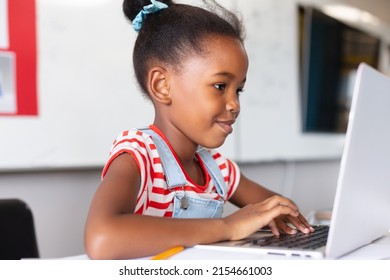 Smiling african american elementary schoolgirl using laptop at desk while studying in class. unaltered, education, learning, studying, concentration, wireless technology and school concept. - Powered by Shutterstock