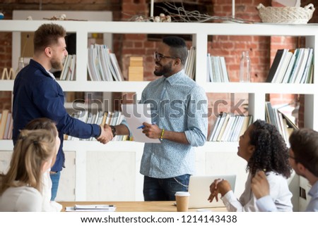 Smiling African American employer handshake millennial worker greeting with good work result during meeting, happy black CEO shake hand of Caucasian employee congratulating with success at briefing