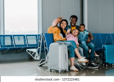 Smiling African American Family With Baggage And Kids Sitting In Airport And Waving Hands Together