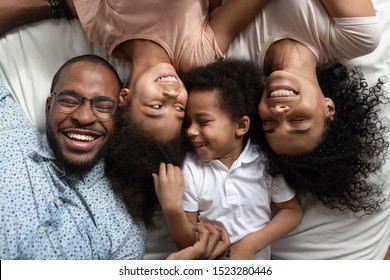 Smiling african american family of four lying on bed head to head with closed eyes, happy parents relaxing with kids elder girl and smaller boy on bed, enjoying weekend leisure free time spending.