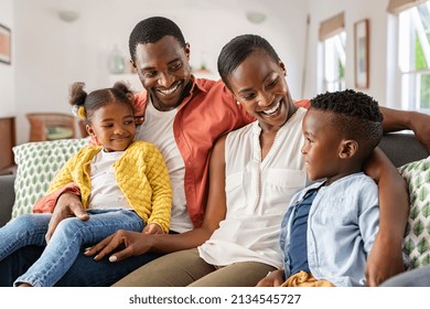 Smiling African American Family Relaxing On Couch And Talking To Each Other. Happy Black Father And Mother Sitting On Sofa At Home With Their Daughter And Son. Playful Ethnic Family With Two Kids.