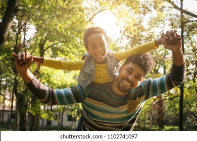 Smiling African American Father Carrying His Daughter On Piggyback And Holding Hands.