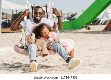 Smiling African American Father And Daughter On Spider Web Nest Swing At Amusement Park 