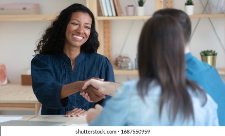 Smiling African American Female Real Estate Agent Shake Hand Grating Getting Acquainted With Clients At Meeting, Happy Biracial Woman Consultant Handshake Close Deal Sign Agreement With Young Couple