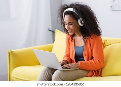 smiling african american freelancer in headphones using laptop in living room - Shutterstock ID 1904135866