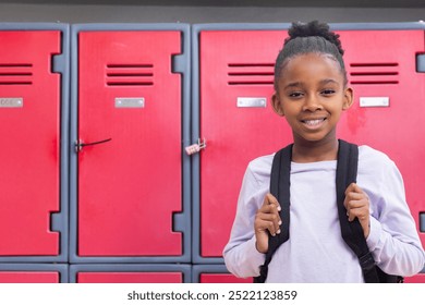 Smiling african american girl with backpack standing in front of red lockers at school, copy space. Education, student, schoolgirl, hallway, teengirl, adolescence - Powered by Shutterstock