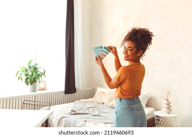 Smiling African American girl stands back to camera in middle of bed room with palette of blue shades for interior renovation, choosing paint for balance of mind and body, refreshing indoor design - Powered by Shutterstock