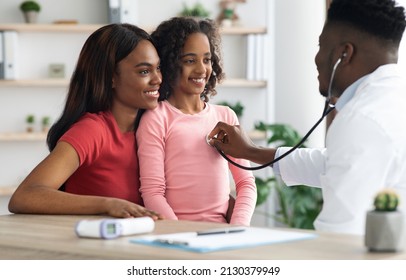 Smiling African American Girl Visiting Doctor At Clinic, Sitting With Her Mother In Front Of Pediatrician, Black Man In Uniform Doc Listening To Child Patient Breath With Stethoscope, Panorama