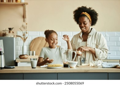 Smiling African American girl and young mother making banana smoothie on large counter having fun and sharing happy moments at cozy beige kitchen, copy space - Powered by Shutterstock