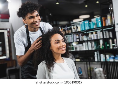Smiling african american hairstylist standing near young woman