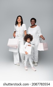 Smiling African American Kid With Mother And Granny Holding White Shopping Bags On Grey