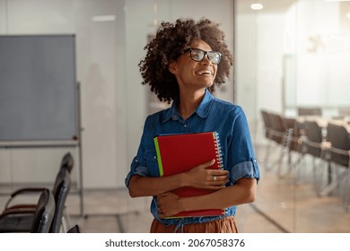 Smiling African American lady holding a notebook with documents with two hands in meeting room