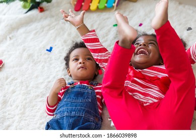 Smiling African American Little Girl And Little Toddler Boy Playing Together On Christmas While Lying On Floor At Home. Merry Christmas And Happy Holidays