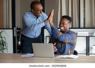Smiling African American male colleagues give high five celebrate shared business victory or win. Happy ethnic men employees triumph for company success or good job results. Teamwork concept.