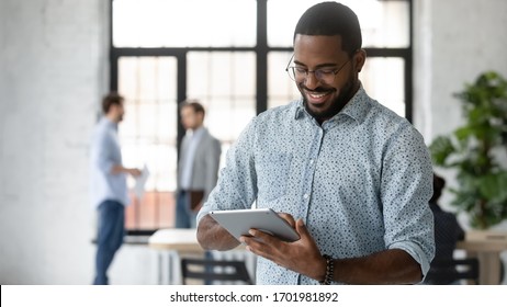 Smiling African American male employee use modern tablet gadget with wireless Internet connection at workplace, happy confident biracial man worker texting or messaging on Pad device in office - Powered by Shutterstock