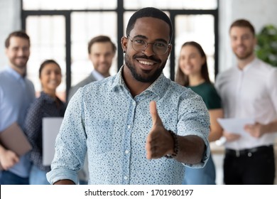 Smiling African American male employer in glasses stretch hand welcome new employee or intern in office, happy biracial boss or businessman meet greet newcomer at workplace, employment concept