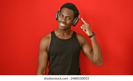 Smiling african american man in black tank top wearing headphones and pointing to his head against a red background. - Powered by Shutterstock