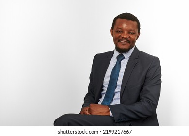 Smiling African American  Man In Business Suit Sitting On Chair Isolated White Background. Happy Executive Businessman, Chief Executive Officer Satisfied Successful Interview With Applicant