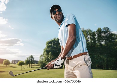 Smiling African American Man In Cap And Sunglasses Holding Club And Playing Golf   