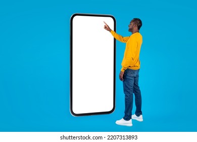 Smiling African American Man In Casual Outwear Touching With Finger Big Smartphone White Blank Screen And Smiling, Black Guy Using Mobile Application Or Surfing On Internet, Mockup, Copy Space