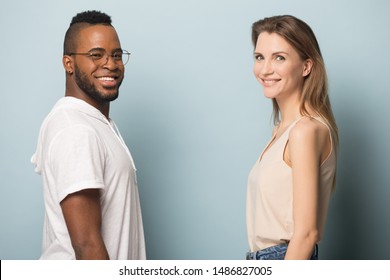 Smiling African American Man And Caucasian Woman Stand Face To Face Isolated On Blue Studio Background Look At Camera, Happy Multiracial Young People Posing Together, Center Blank Copy Space