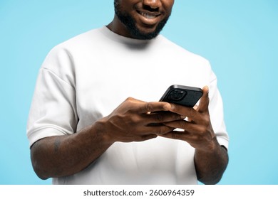 Smiling African American man holding mobile phone using mobile app on blue background, selective focus on hands. Online technology concept