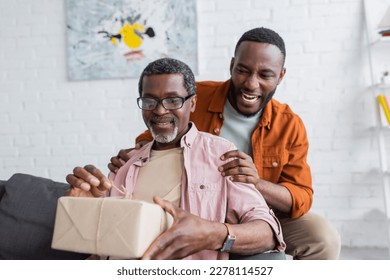 Smiling african american man hugging dad with gift during father day at home