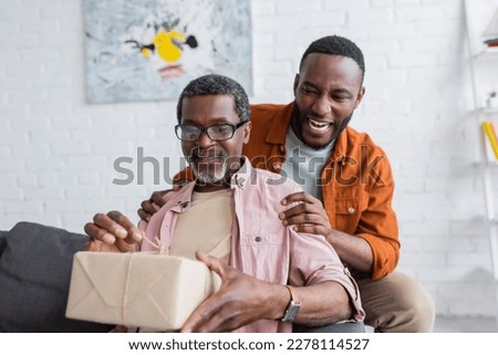 Smiling african american man hugging dad with gift during father day at home