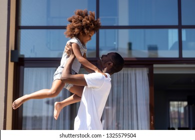 Smiling African American Man Lifting Up Daughter, Happy Laughing Father Playing Funny Game With Adorable Child, Little Girl Outdoor In Yard, Family Spending Free Time, Weekend Together