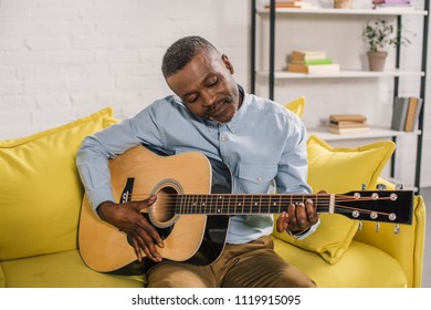 smiling african american man playing acoustic guitar at home - Powered by Shutterstock