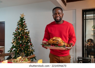 Sonriente afroamericano con suéter rojo celebrando Navidad con pavo asado para cenar en casa