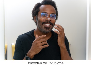 smiling African American man reflect in mirror apply cleanse products on face or facial cream, put moisturizing or nourishing creme, enjoy soft hydrated skin. Skincare, personal hygiene routine - Powered by Shutterstock