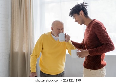 Smiling African American Man Standing Near Granddad Drinking Tea At Home