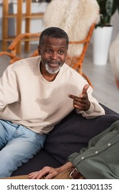 Smiling African American Man Talking To Blurred Elderly Friends On Couch