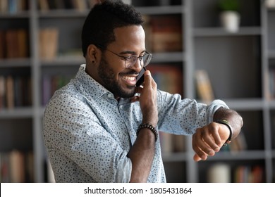 Smiling African American man wearing glasses checking time while making phone call close up, confident positive businessman planning meeting with partner, looking at wristwatch, task management - Powered by Shutterstock